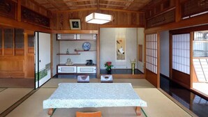 Una habitación con esterillas de tatami, una mesa baja, cojines naranja y una lámpara colgante.