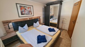 Habitación de hotel con dos camas, cabecero de madera, una obra de arte enmarco, espejo y armario.