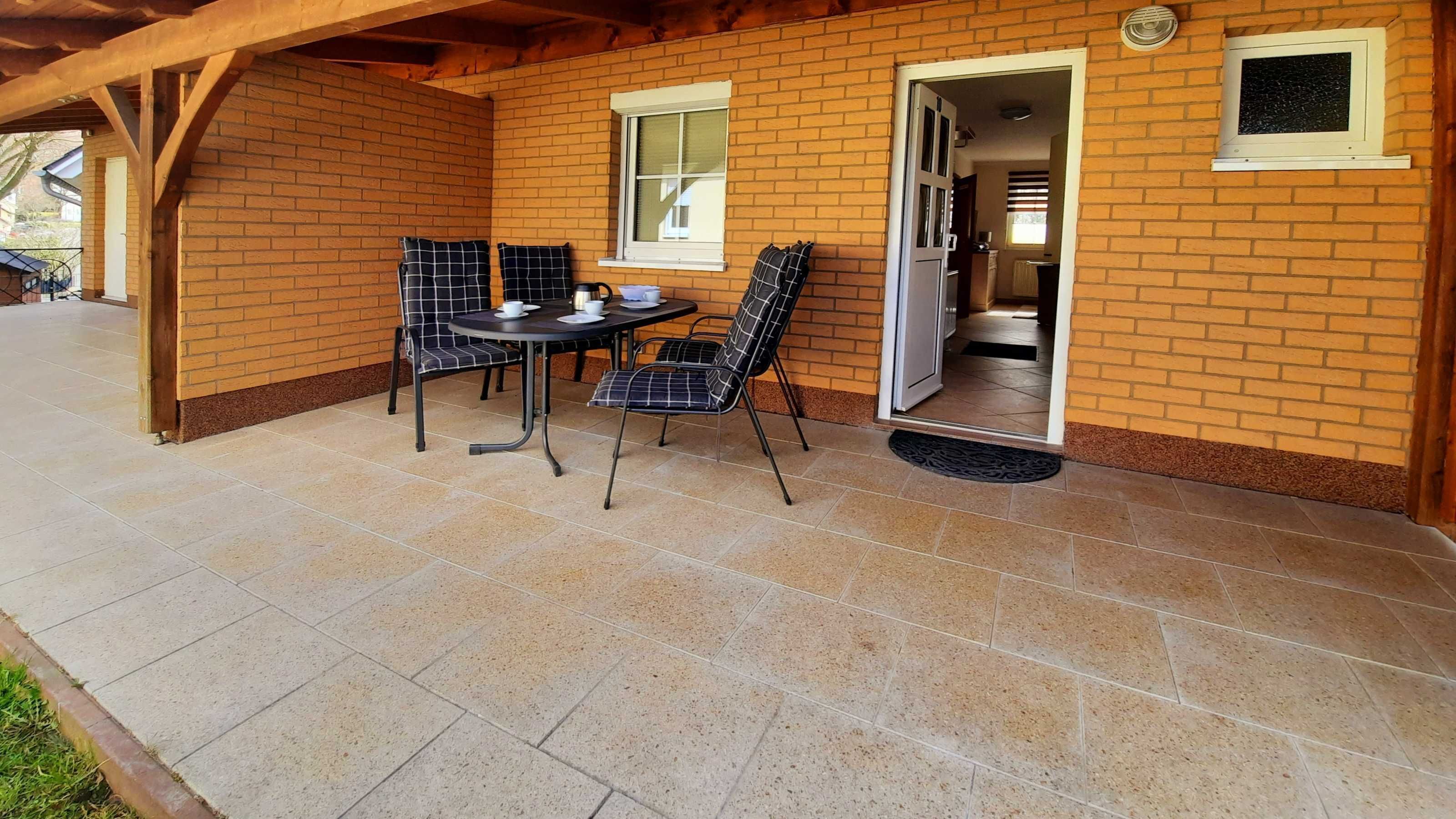 A covered patio area with a brick wall, a table with chairs, and a door leading to an interior space.
