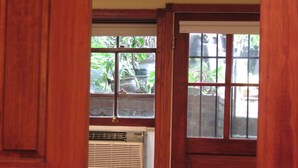 Una habitación con puerta de madera, ventana con persianas y equipo de aire acondicionado.