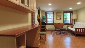 Una habitación con escritorio de madera, una silla, un sofá, un televisor y una ventana con vistas a zonas verdes.