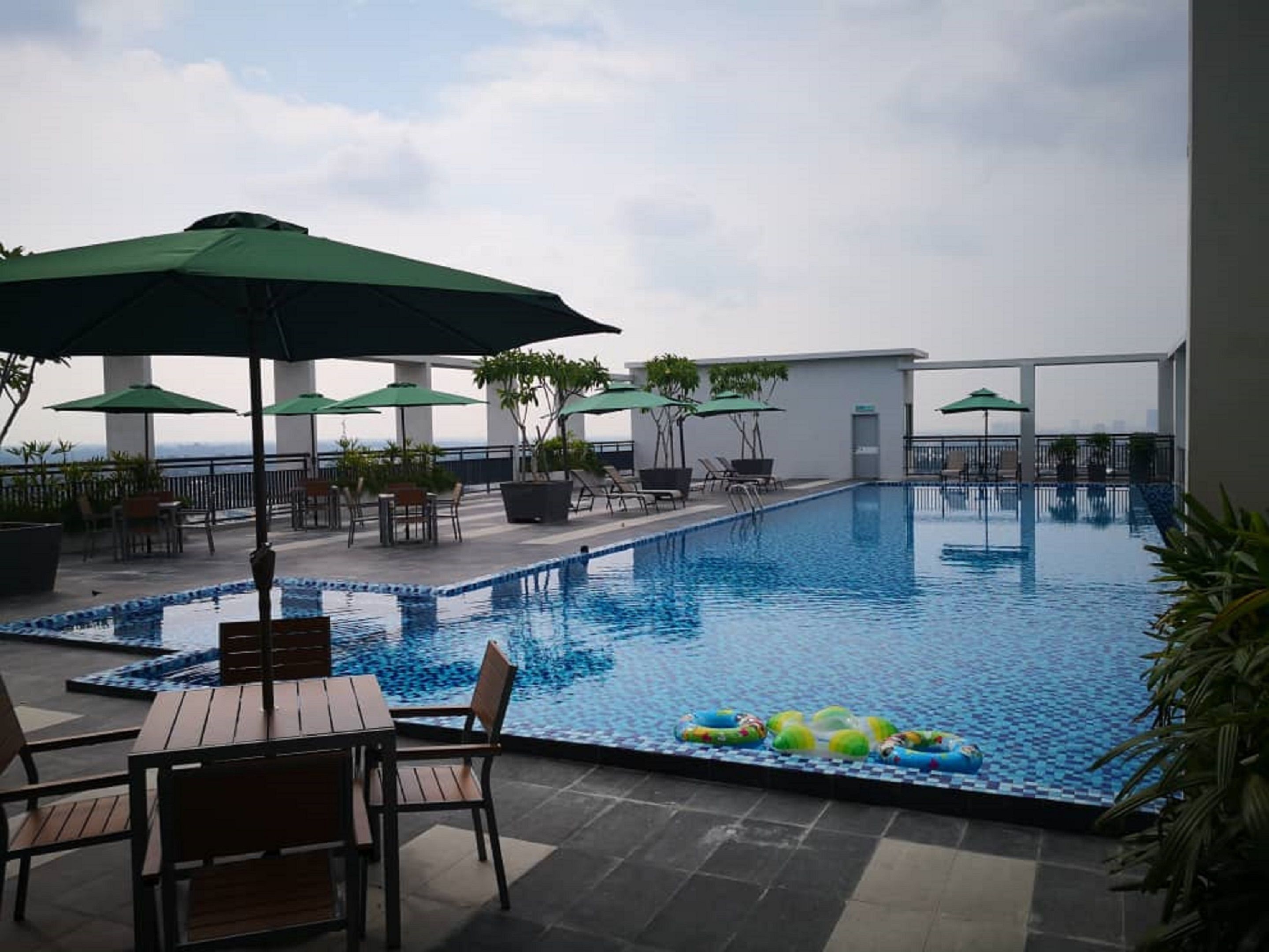A rooftop pool with lounge chairs and umbrellas, surrounded by potted plants and a view of the city skyline.