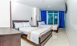 A hotel room with two beds, a desk, a phone, and a window with blue curtains.