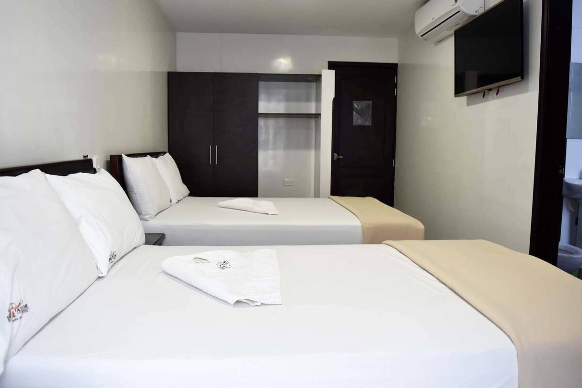 Habitación de hotel con dos camas, un armario, un televisor y un equipo de aire acondicionado.
