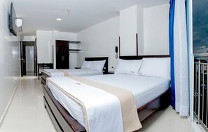 A hotel room with two beds, a wardrobe, a flat-screen TV, and a view of the sea.