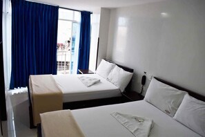 A hotel room with two beds, a window with blue curtains, and a view of a building outside.