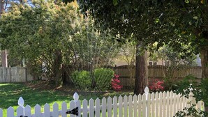 A white picket fence with a gate, surrounded by lush greenery and trees. - Super Location. Close to about everywhere .Great value.Over 200 reviews!! (Richmond)