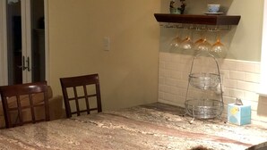 A kitchen with a granite countertop, a chair, a hanging light fixture, and a shelf with decorative items. - Super Location. Close to about everywhere .Great value.Over 200 reviews!! (Richmond)