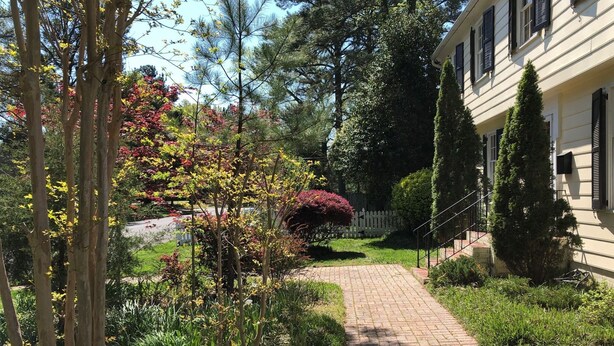 A garden pathway leading to a building with a white facade and black shutters. - Super Location. Close to about everywhere .Great value.Over 200 reviews!! (Richmond)