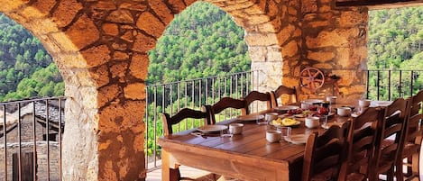 Zona de dinar amb parets de pedra i taula preparada per a sis, amb vista a un paisatge forestal.