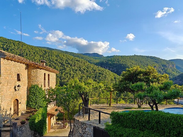 A stone building with a patio, surrounded by lush greenery and mountains.