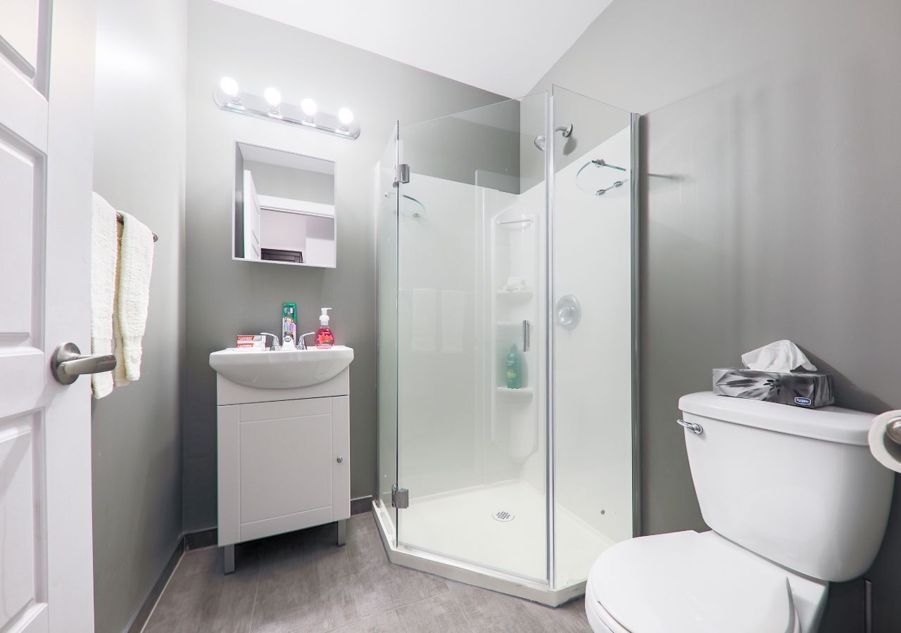 A modern bathroom with a glass-enclosed shower, a white sink with a mirror above, and a toilet.