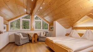 A bedroom with a wooden ceiling, a bed, a desk, two chairs, and large windows. - Apartment Sterngucker - Guesthouse Herrmann (Filzmoos)