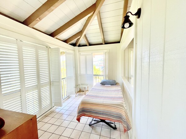 Una habitación estrecha con cama, una mesita y una ventana con persianas.