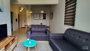 A modern living room with a flat-screen TV, a sofa, a coffee table, and a dining area with a table and chairs. - Arcadia Penang by Plush (George Town)