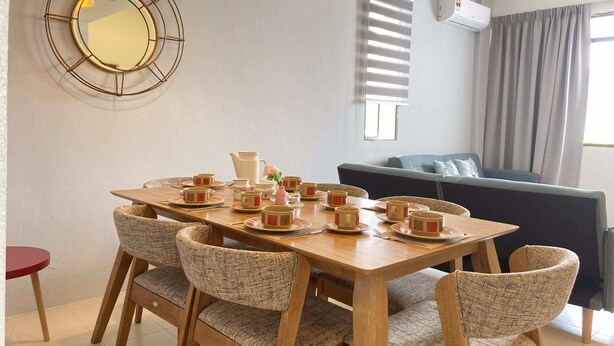 A dining area with a wooden table set for four, surrounded by four upholstered chairs. A round mirror hangs on the wall above the table. - Arcadia Penang by Plush (George Town)