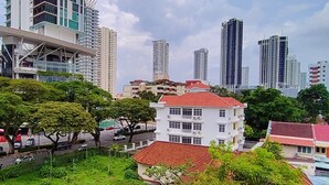 A cityscape with modern high-rise buildings, a white building with a red roof, and a street with vehicles and trees. - Arcadia Penang by Plush (George Town)