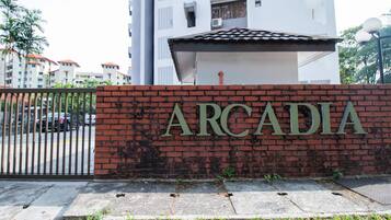 A brick wall with the name "ARCADIA" in large letters, a gated entrance, and a modern building in the background.