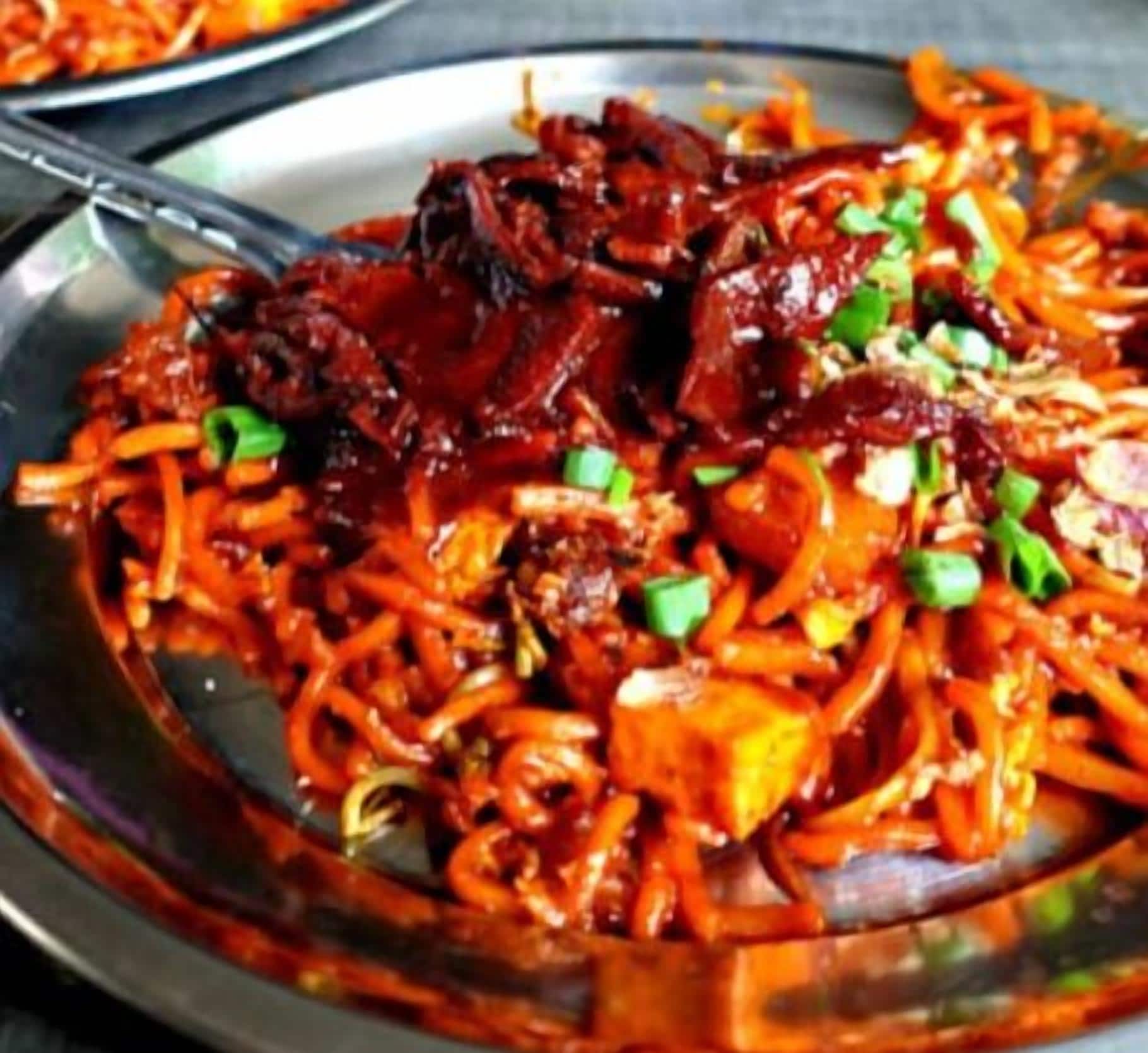 A plate of stir-fried noodles with vegetables and meat, garnished with green onions.