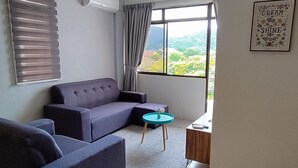 A living room with a sofa, armchair, and a small table. There are two framed motivational posters on the wall. - Arcadia Penang by Plush (George Town)