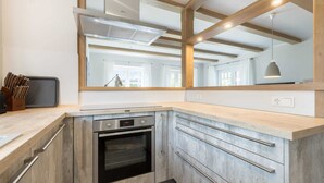 Une cuisine moderne dotée d’un four encastré, d’appareils électroménagers en acier inoxydable et d’un grand miroir au-dessus du plan de travail.