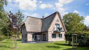 Une maison en pierre avec un toit en pente, un balcon et un patio aménagé avec des sièges d’extérieur.