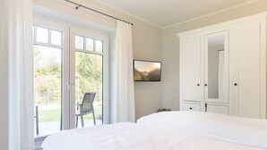 Une chambre avec un grand lit, une porte-fenêtre coulissante donnant sur une terrasse, un fauteuil et un téléviseur fixé au mur.