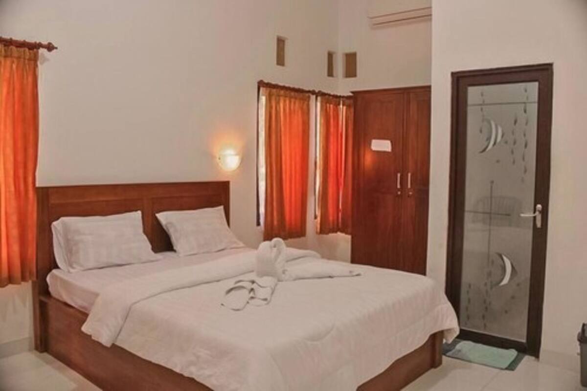 A hotel room with a bed, curtains, a wardrobe, and a door.