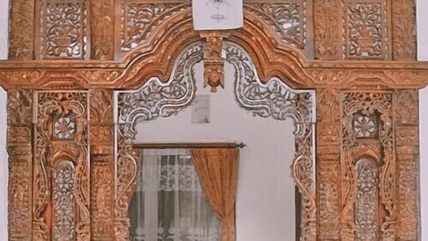 A mirror with ornate wooden carvings and a white cloth hanging above it.