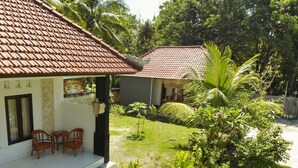 A house with a tiled roof, a small garden with palm trees, and a balcony with wooden chairs.