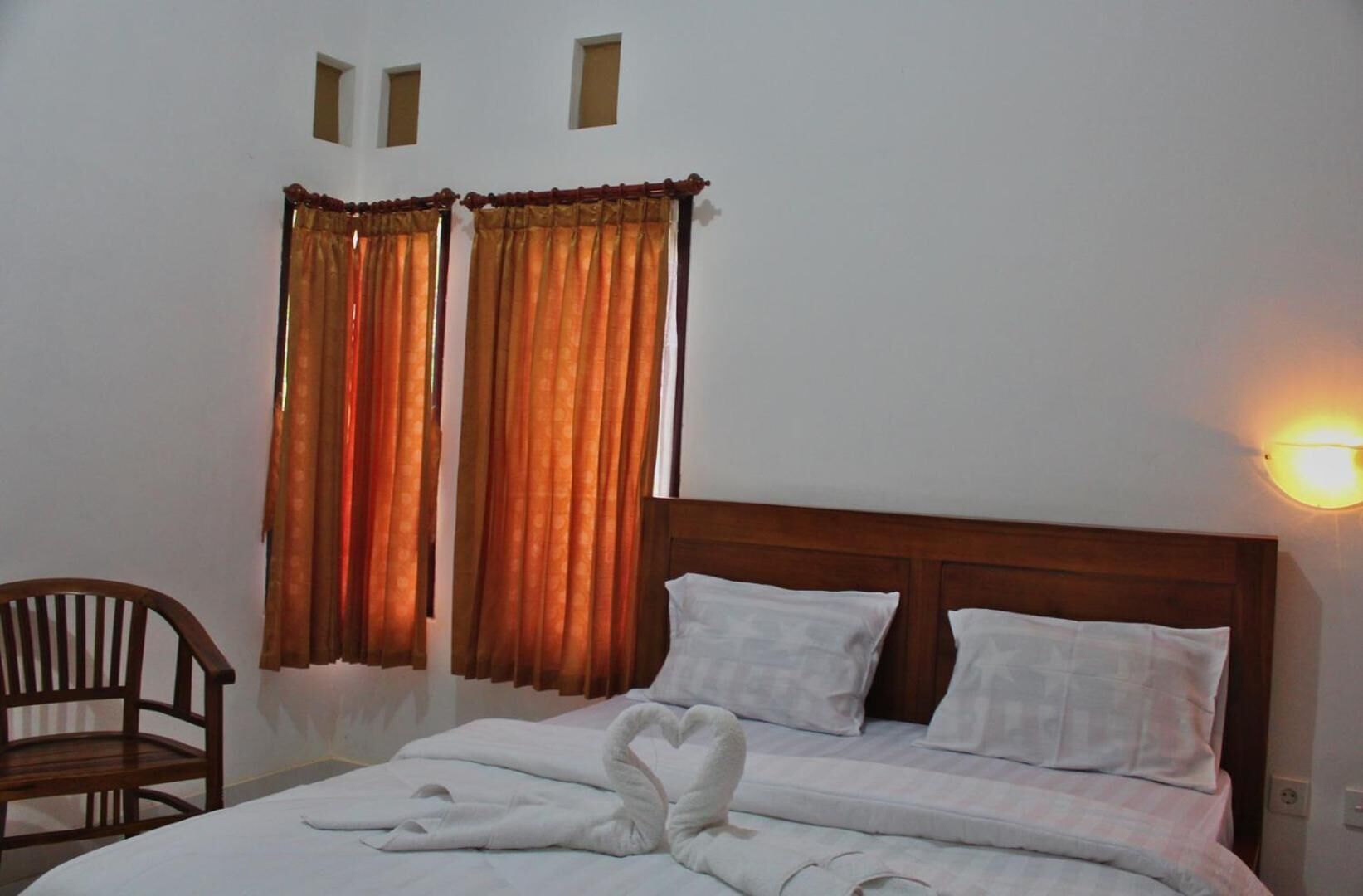 A hotel room with a bed, two pillows, a wooden headboard, a chair, and curtains.
