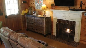 Een knus interieur van een chalet met een open haard, houten wanden, een televisie erboven en een comfortabele bank.