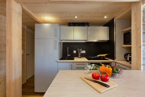 A modern kitchen with wooden cabinetry, a black countertop, and a wooden table with fresh vegetables.