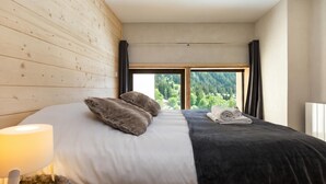 A bedroom with a bed, a lamp, a window, and a view of greenery. - Grand Roc C411 280m from Slopes, Mont-Blanc View, Parking & WiFi, Argentière (Chamonix), France (Argentière (Chamonix))