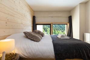 Ein Schlafzimmer mit Bett, Lampe, Fenster und Blick ins Grüne.