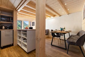 Eine moderne Küche mit Mikrowelle, Wasserkocher und Kaffeemaschine, ein Essbereich mit Tisch und Stühlen sowie Blick ins Freie.