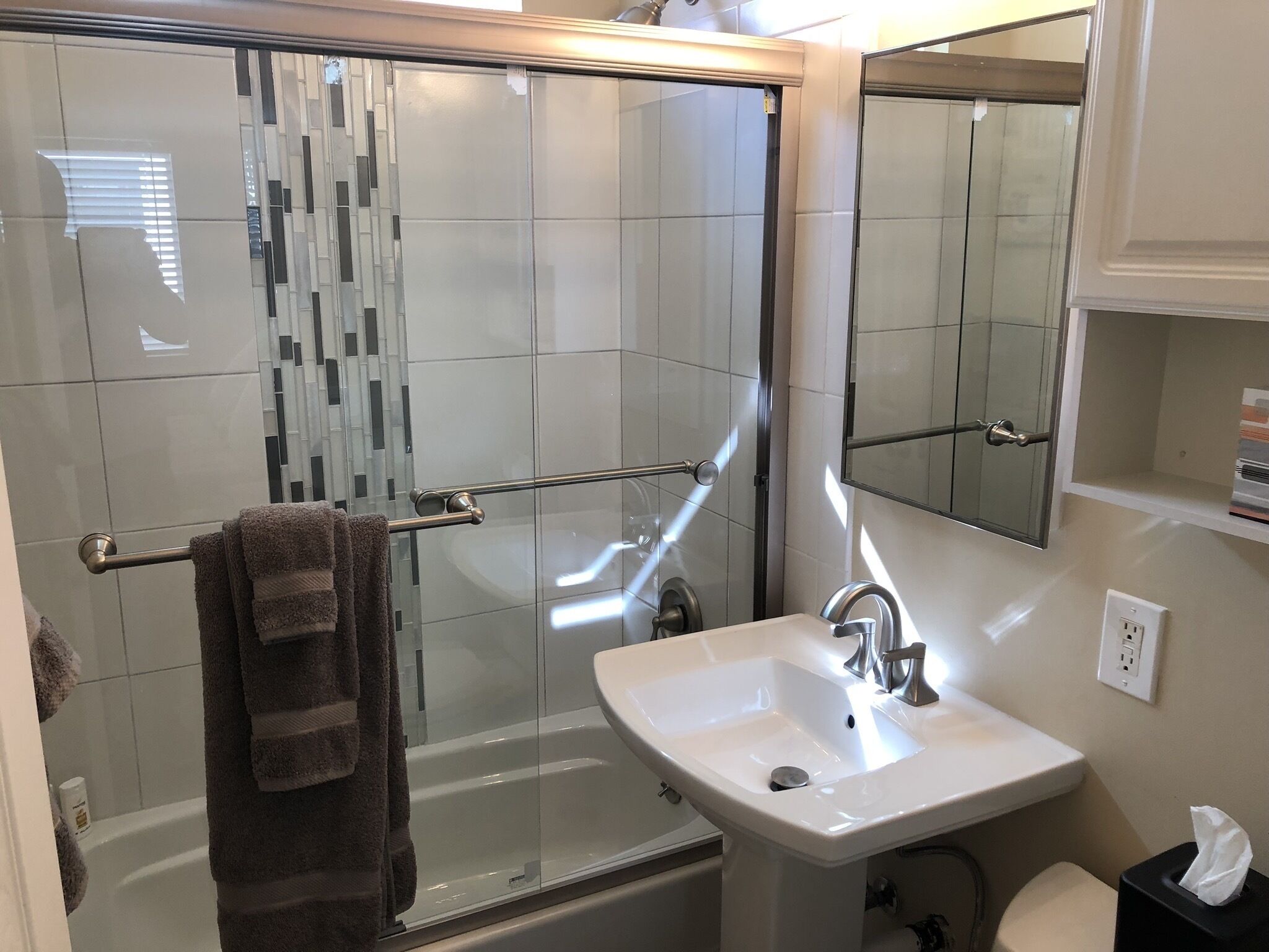 A bathroom with a glass shower enclosure, a white sink, and a mirror above the sink.