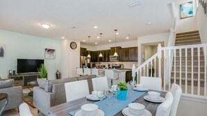 Un salon moderne comprenant un coin repas, une cuisine et un escalier.