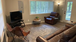Een woonkamer met een televisie, leren fauteuils, een salontafel en een raam met zonwering.