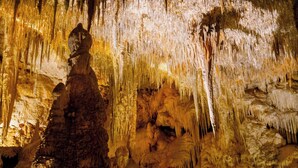 A cave with stalactites and stalagmites, illuminated by artificial lighting.