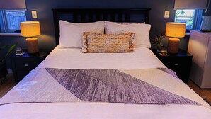 A neatly made bed with a patterned throw, two bedside lamps, and a nightstand with a small plant.