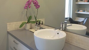 A modern bathroom with two sinks, a large mirror, and a potted orchid.