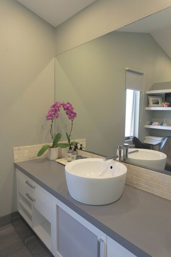 A modern bathroom with two sinks, a large mirror, and a potted orchid.