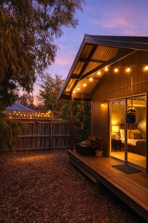 A wooden cabin with a covered porch, string lights, and a bed with pillows.