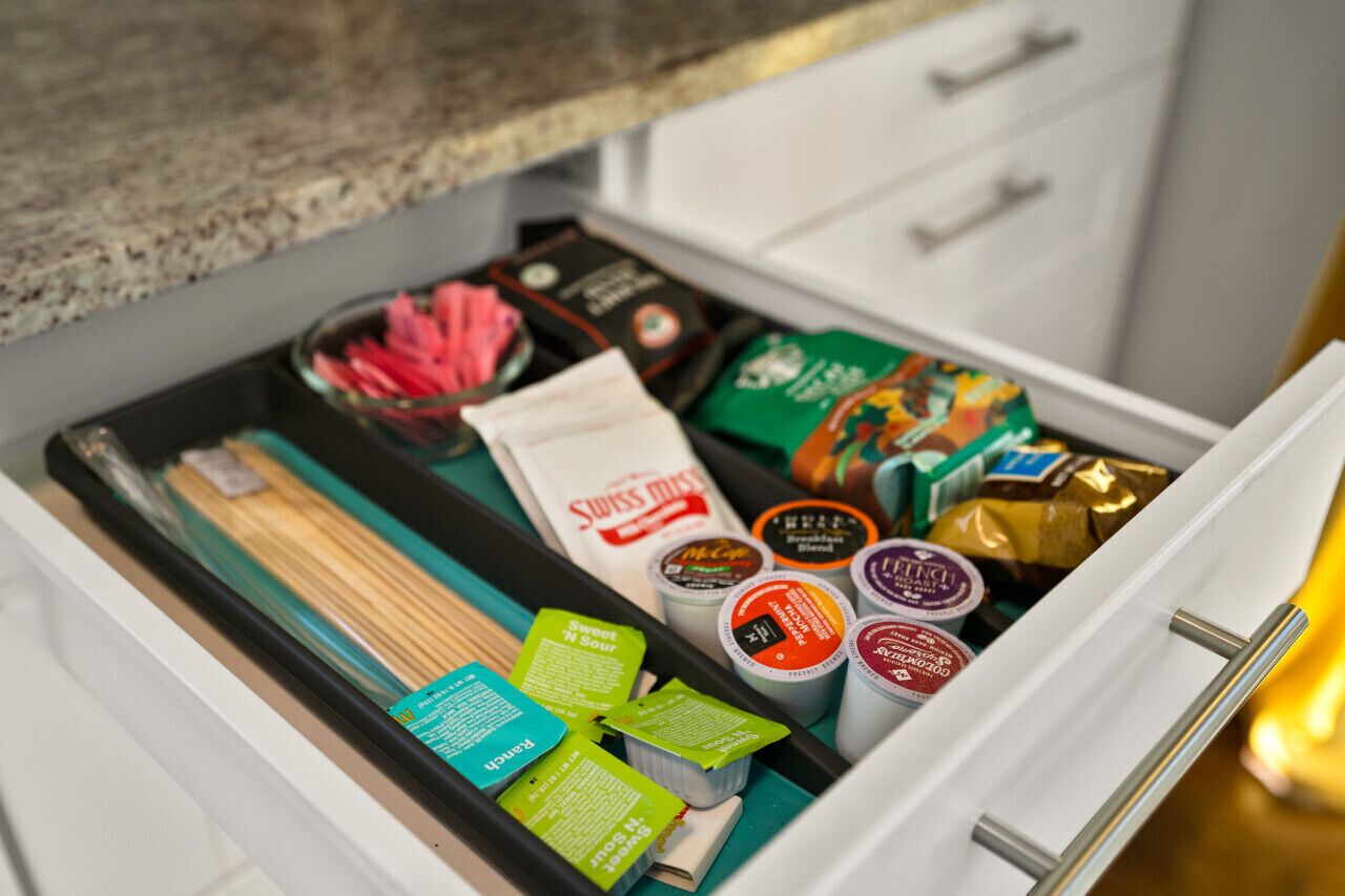 Un tiroir rempli de divers produits alimentaires, notamment des collations emballées, des condiments et un sachet de thé Swiss Miss.