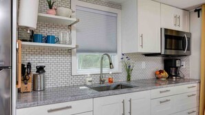 A modern kitchen with white cabinets, a stainless steel refrigerator, a sink, and a microwave.