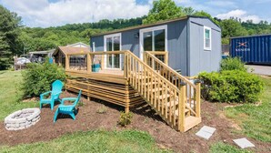 A small, single-story wooden cabin with a deck and a staircase leading to a covered porch.