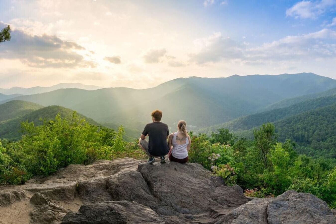 Two people sitting on a rocky outcrop overlooking a mountainous landscape.