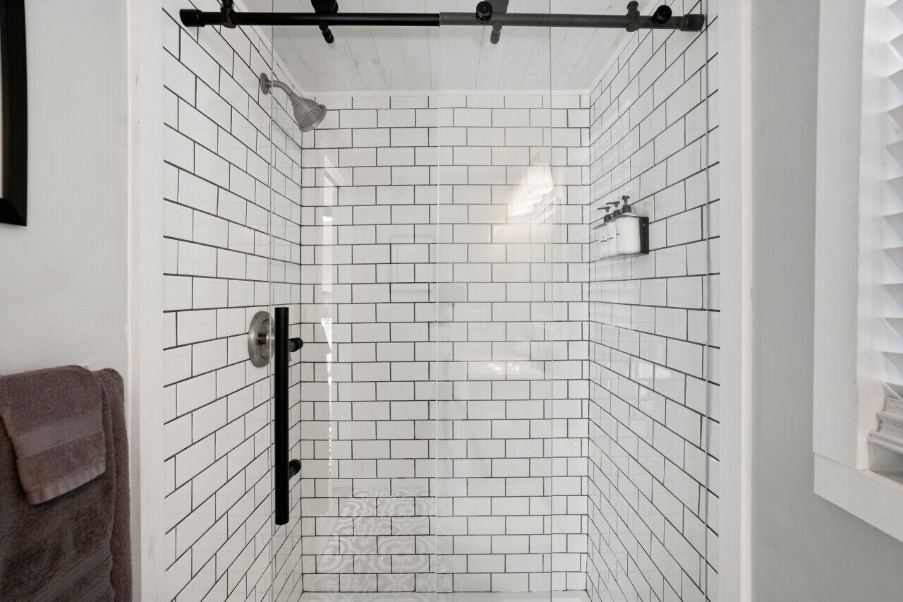 A shower with white tiled walls and a glass door.