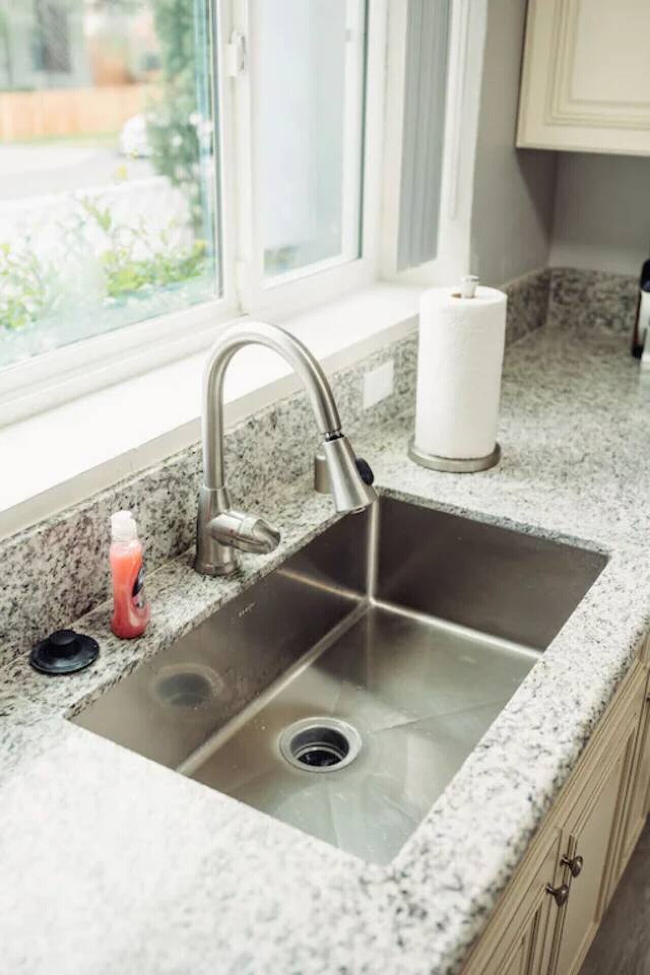 A kitchen sink with a modern faucet, a bottle of dish soap, and a roll of paper towels on the countertop.